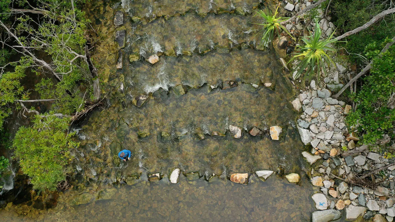 A body of water with five rows of rocks placed horizontally across the waterway