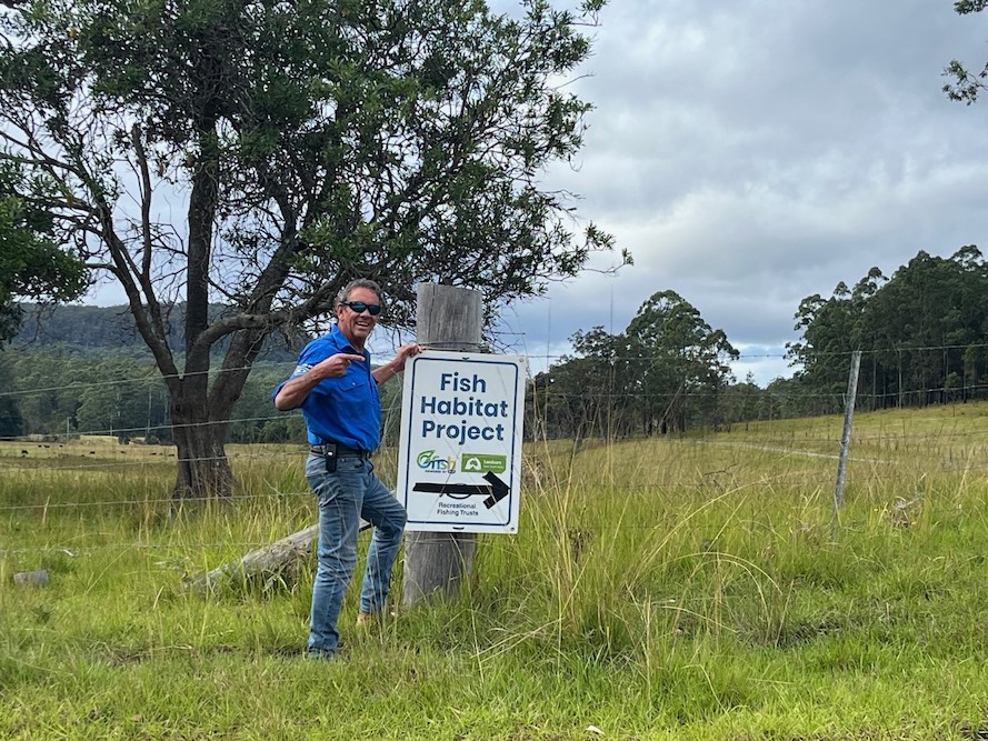 A man in front of a Fish Habitat Project sign