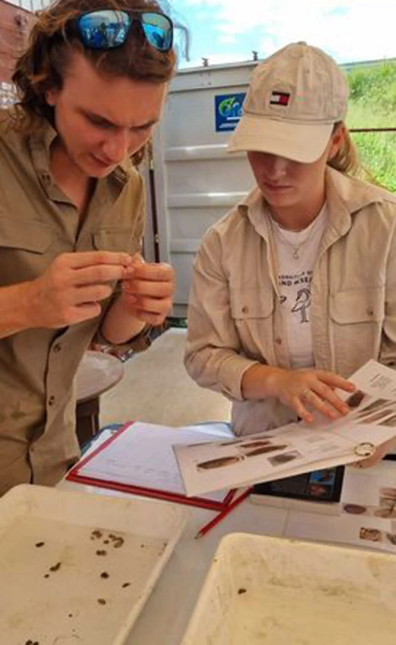 Two people examining a specimen and comparing it to a picture in a book