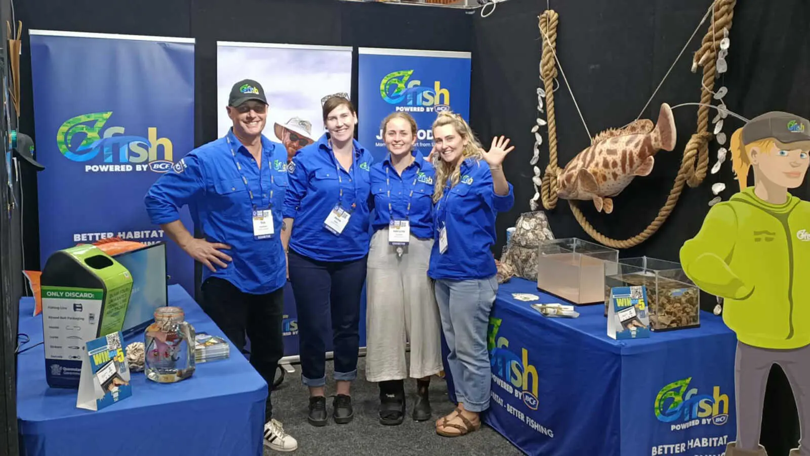 Four people wearing blue shirts standing at an OzFish stall at an expo