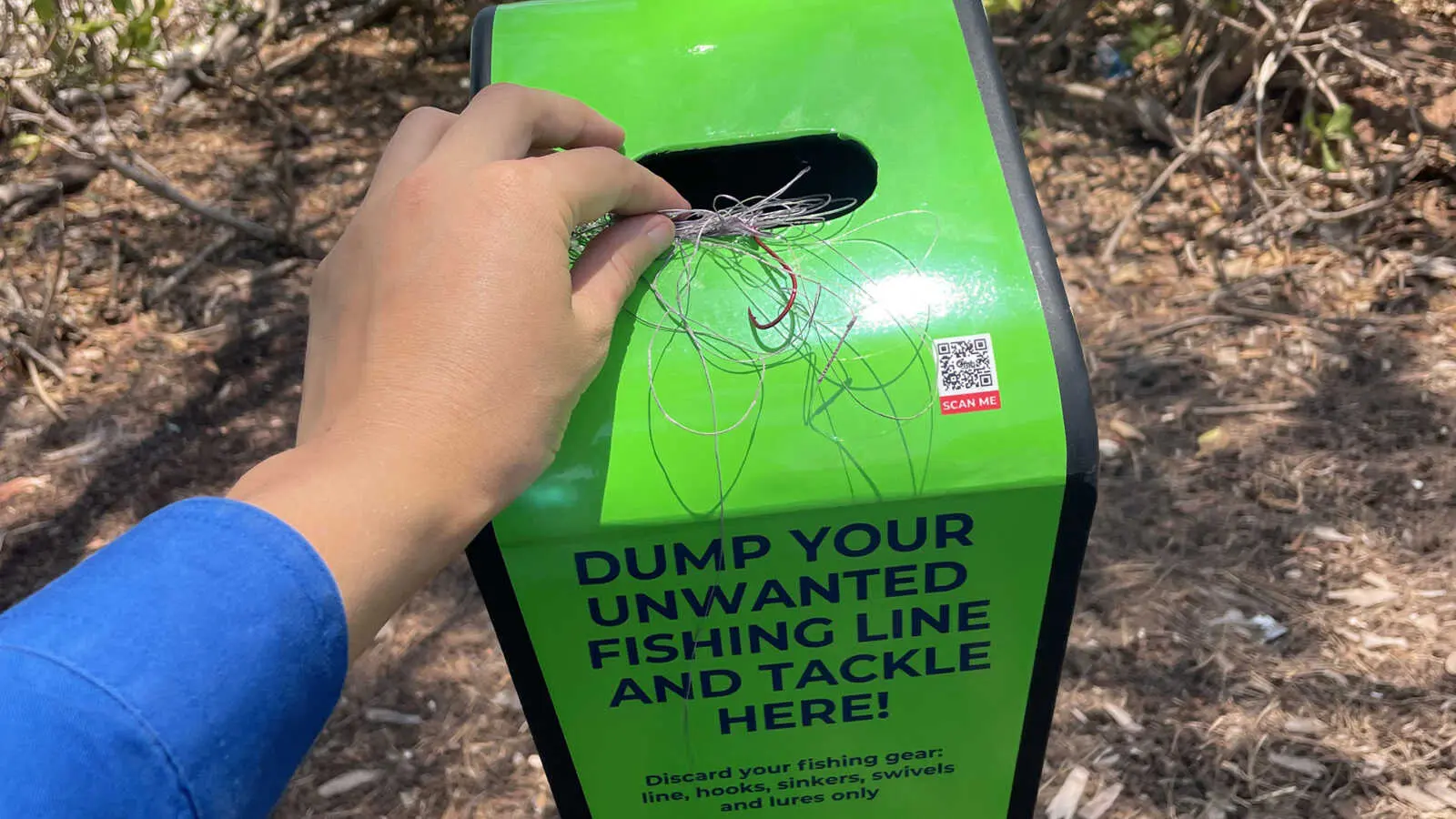a hand putting fishing line into a green tangle bin