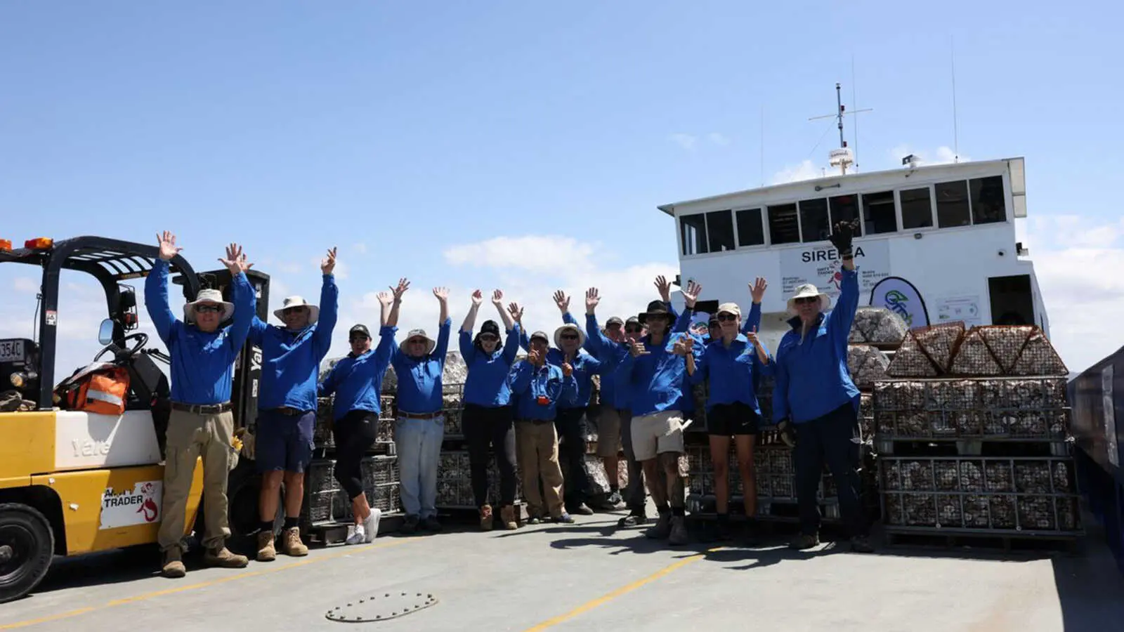 A group of people wearing blue shirts, standing on a boat with their arms in the air