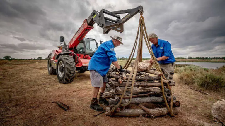 two men securing logs to be transferred by a machine in the background