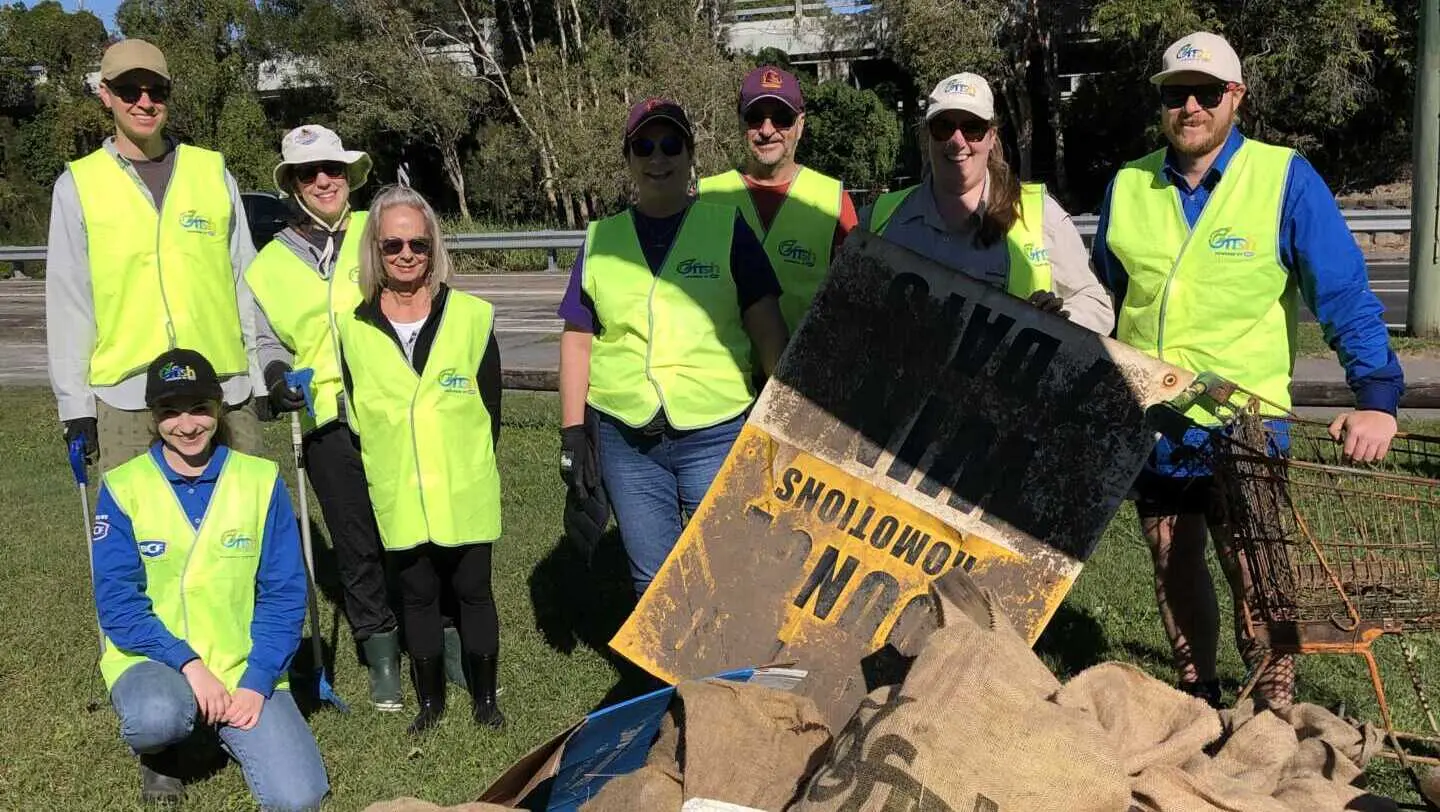 A group of volunteers in high vis vests standing in front of a pile of rubbish they have collected from Saltwater Creek