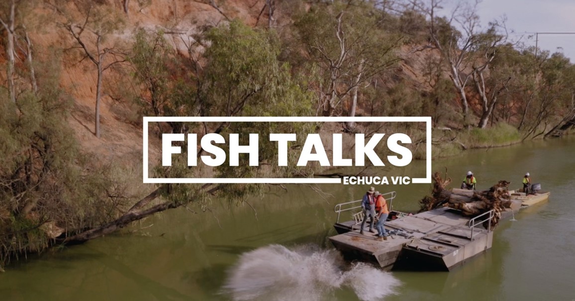 A boat on a river deploying fish habitat with a white Fish Talks Echuca Vic banner in the foreground